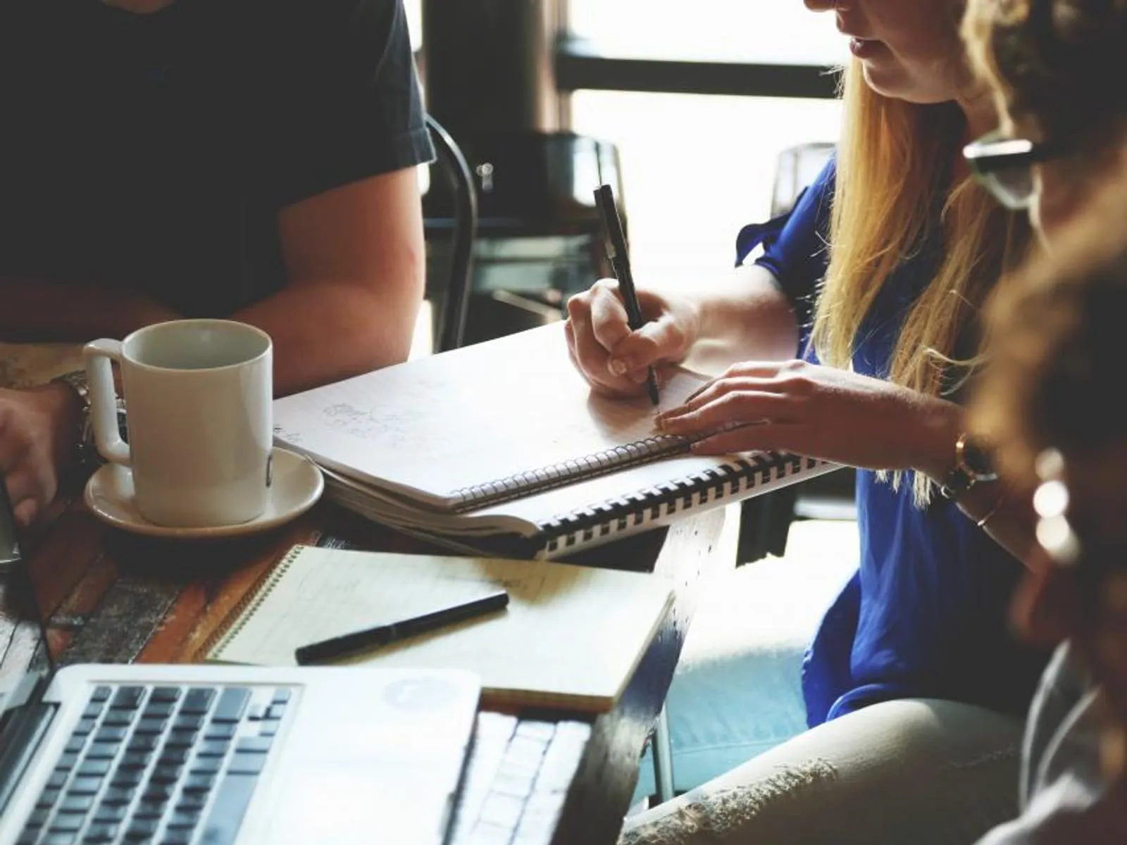 Two people working through written notes at a table with a laptop and coffee.