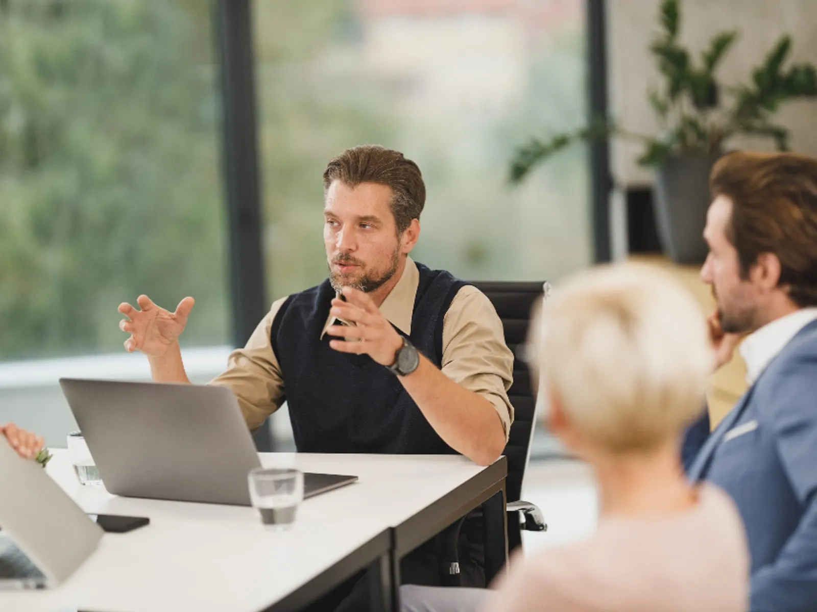 Several people in discussion around a meeting table with open laptops.