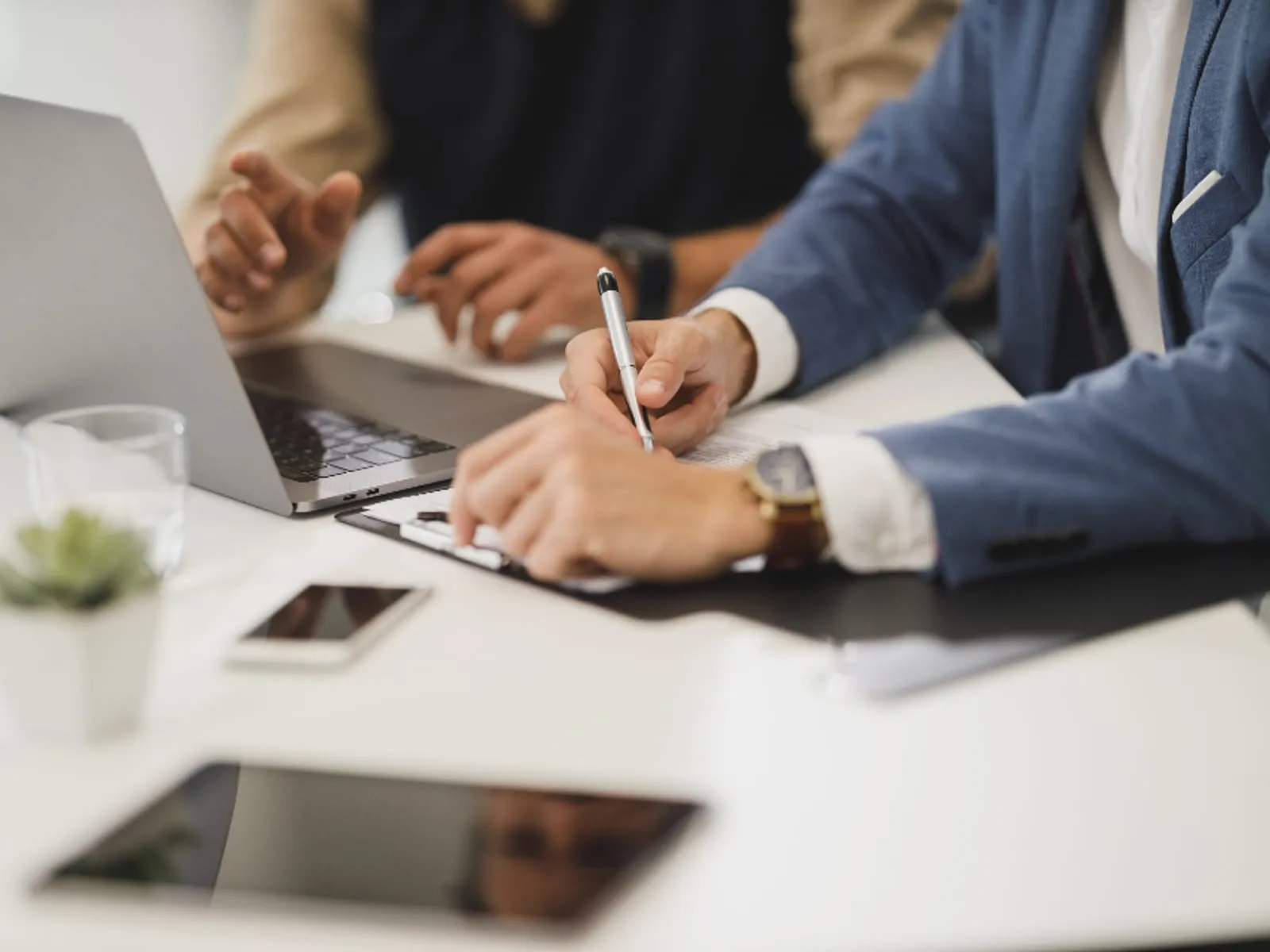 Hands working through printed documents beside a laptop on a desk.