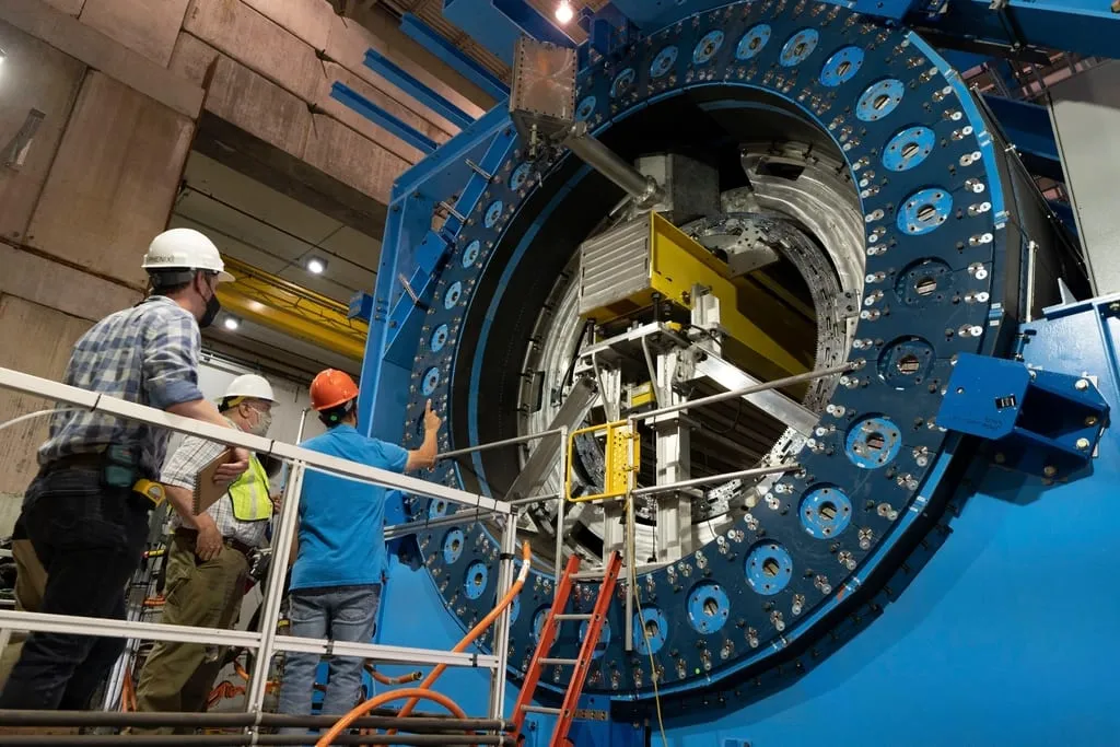 Engineers on a platform working on a large flanged industrial assembly inside a hall.