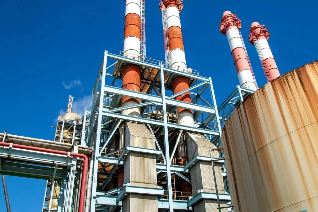 A process plant with steel structure, stacks and storage tanks against a clear sky.