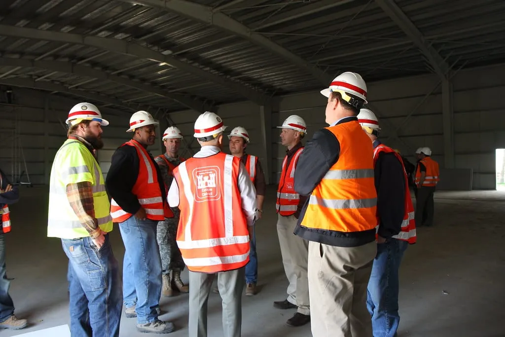 Engineers in hard hats and high-visibility vests talking together inside a newly built hall.