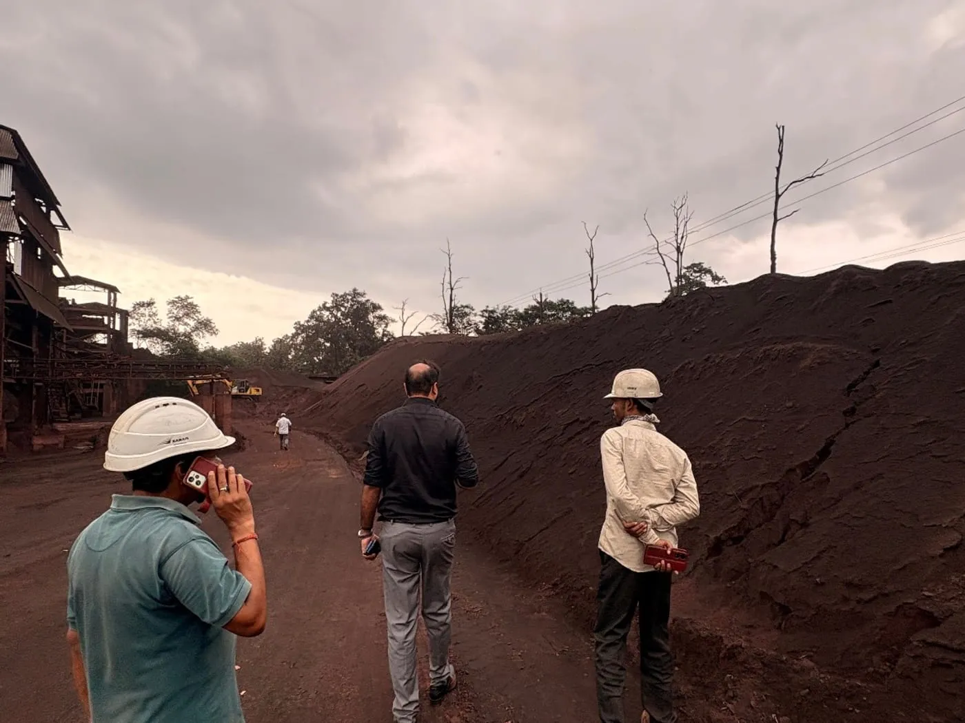 Brikway personnel in hard hats walking a haul road beside stockpiled ore, with a processing plant behind.