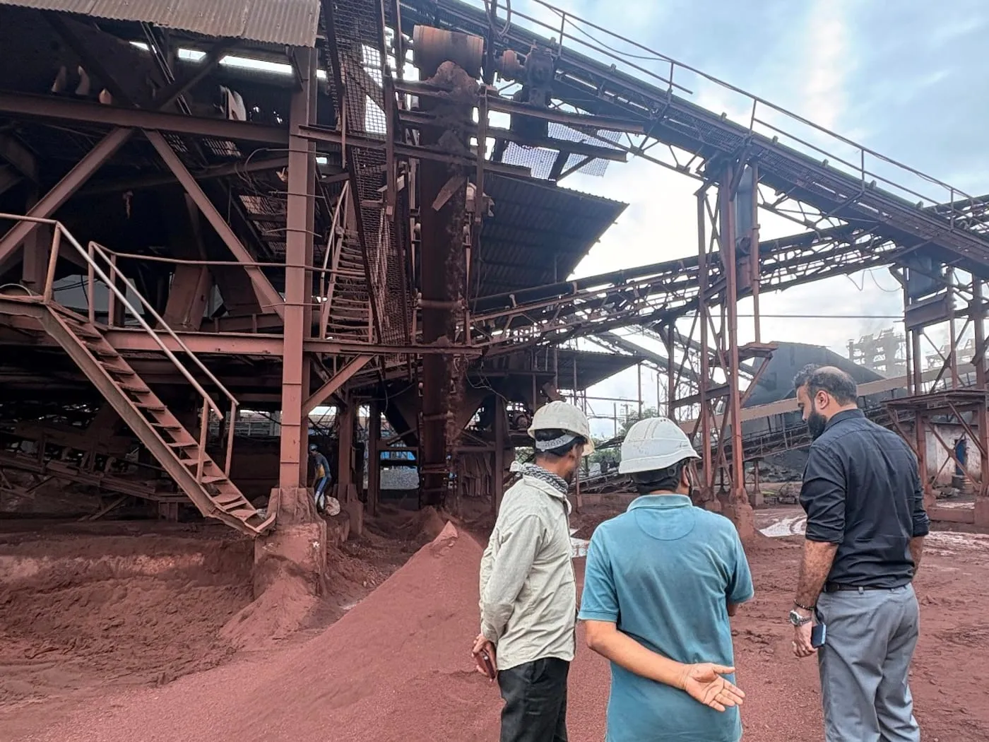 Brikway personnel in discussion in front of a mineral processing plant and conveyor gantry.
